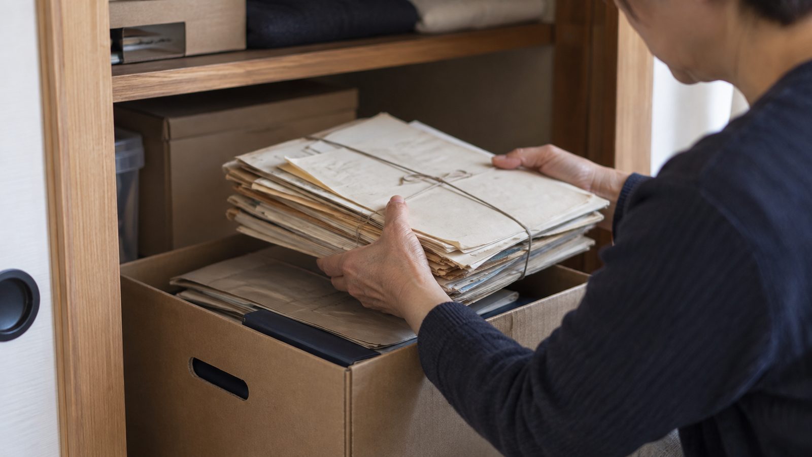 押し入れの書類箱から古い書類の束を取り出している手元